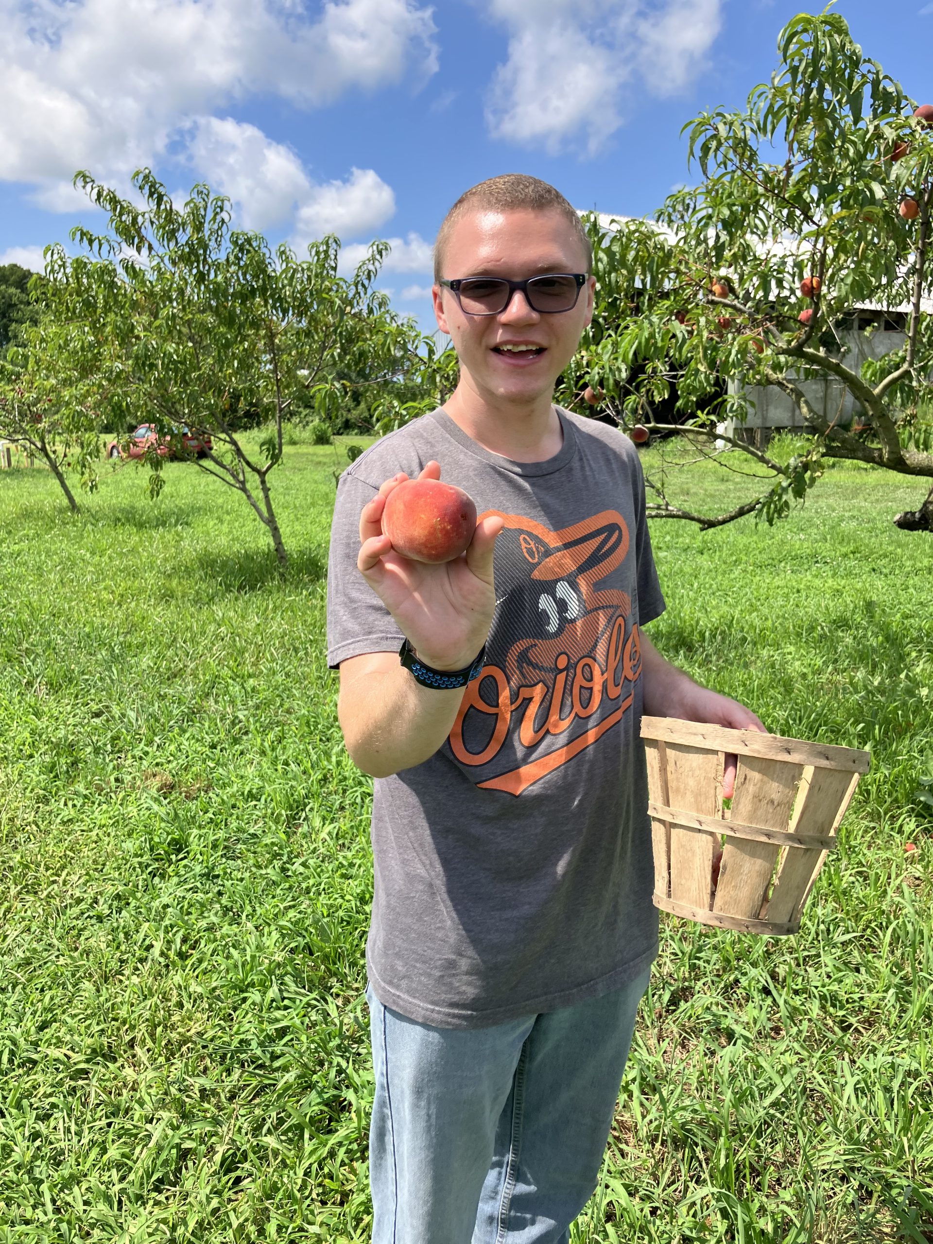 Smiling young man holding a freshly picked peach in an orchard.